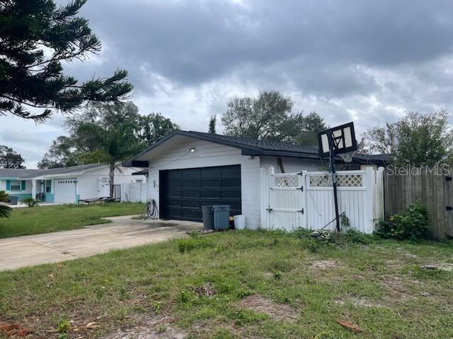 White detached garage with a black door, driveway, basketball hoop, and fenced side yard.