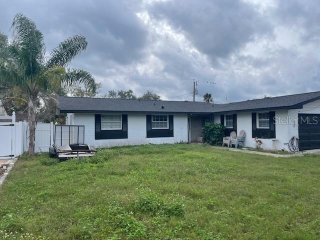 Single-story white home with dark shutters, a grassy yard, palm tree, and outdoor chairs.