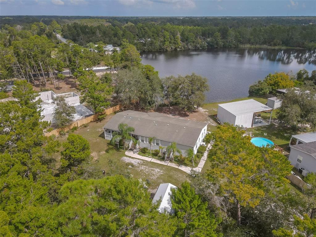 Aerial view of a wooded lakeside home with a swimming pool and detached outbuilding.