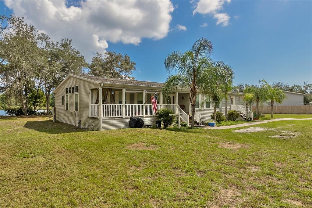 Beige single-story home with a covered porch, palm trees, and a glimpse of water beyond the lawn.