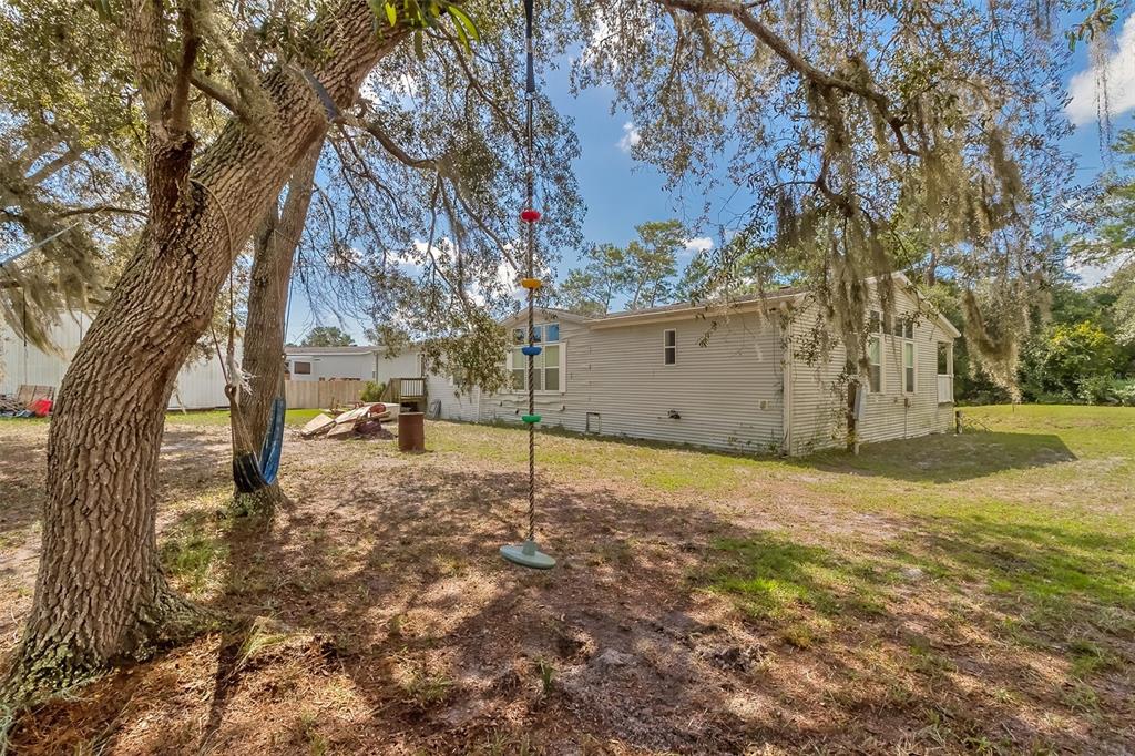 Single-story home beneath moss-draped oak trees, with a hammock in the shady yard.