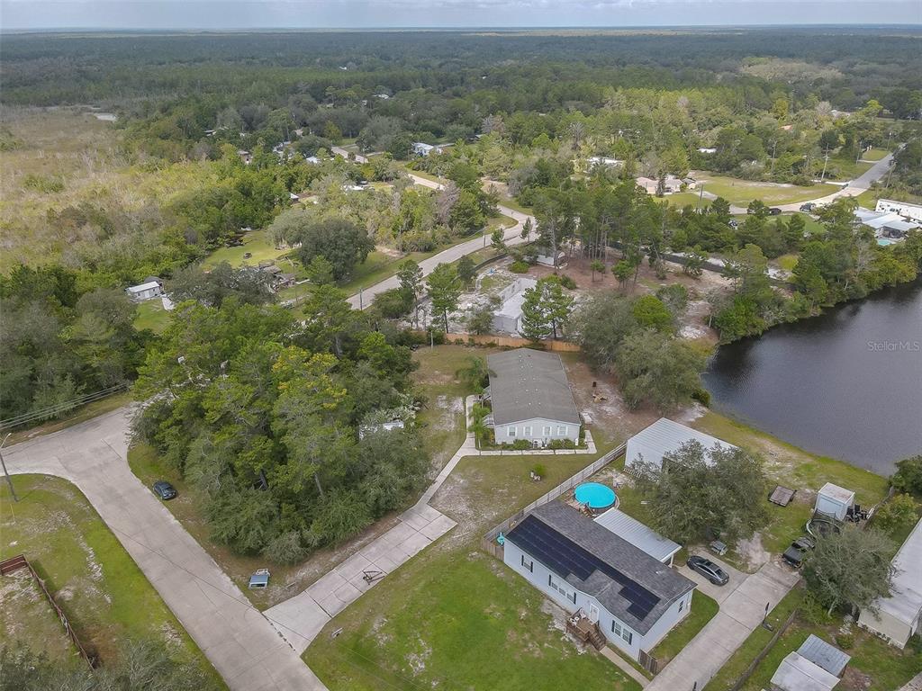 Aerial view of a home with solar panels and a round pool beside a pond.