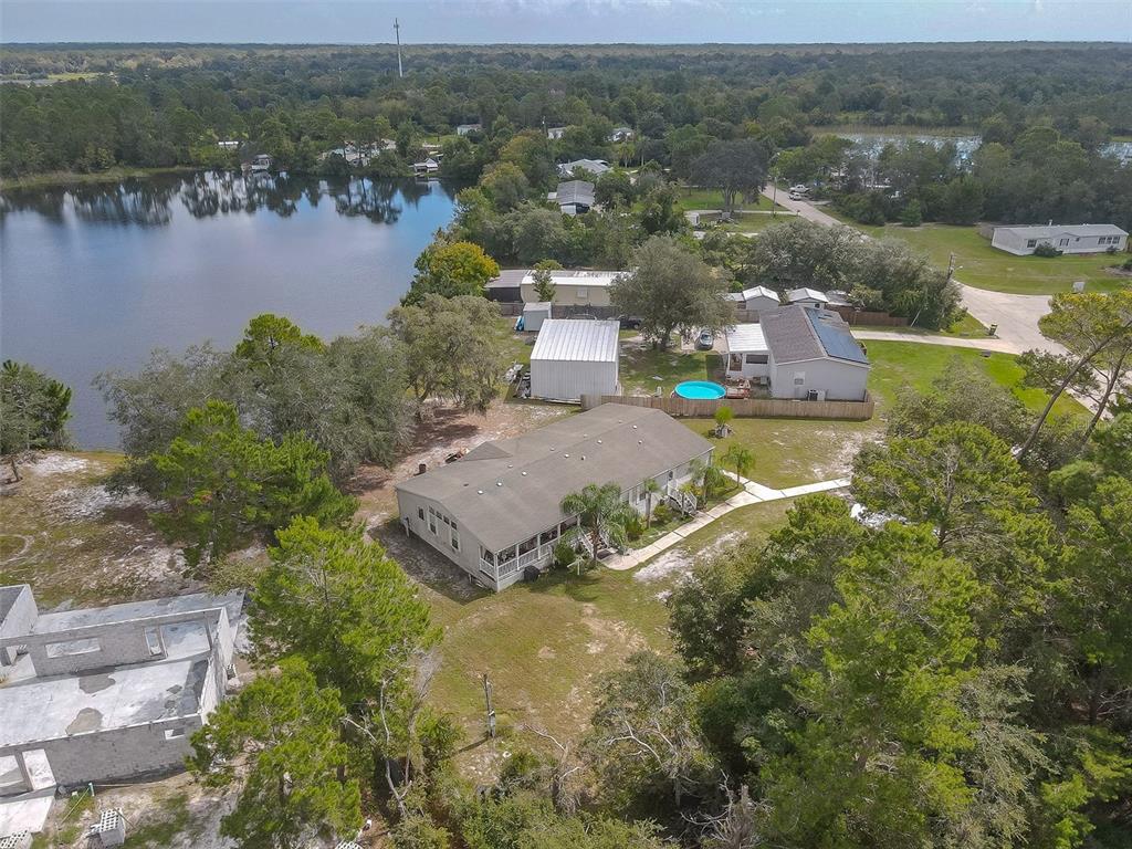 Aerial view of a home beside a lake, with a small blue pool and wooded surroundings.