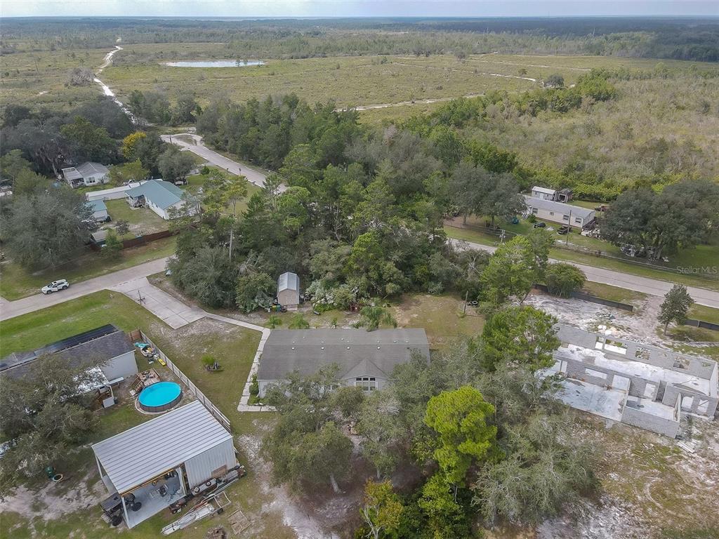 Aerial view of a rural home, detached metal-roofed outbuilding, and round above-ground pool.
