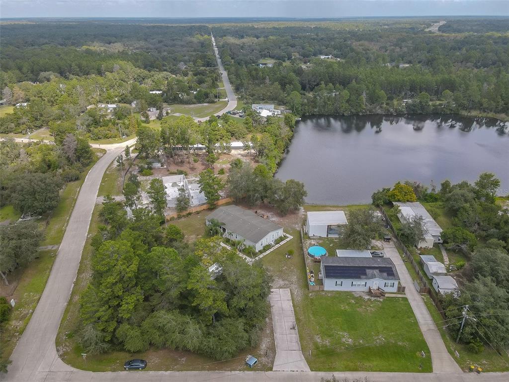 Aerial view of a home beside a lake, with a backyard pool and tree-lined surroundings.