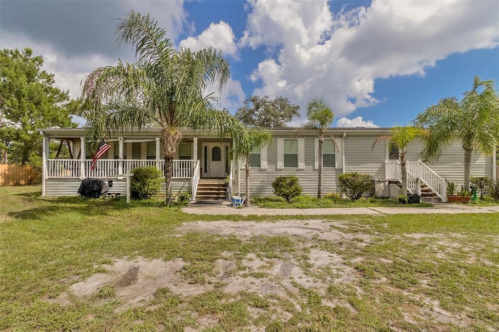 Single-story home with a covered porch, white railings, and palm trees in the yard.