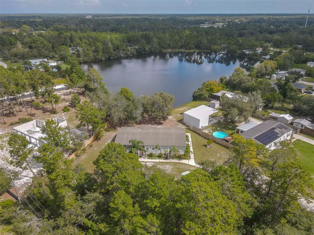 Aerial view of a single-story home beside a lake, with a small backyard pool.