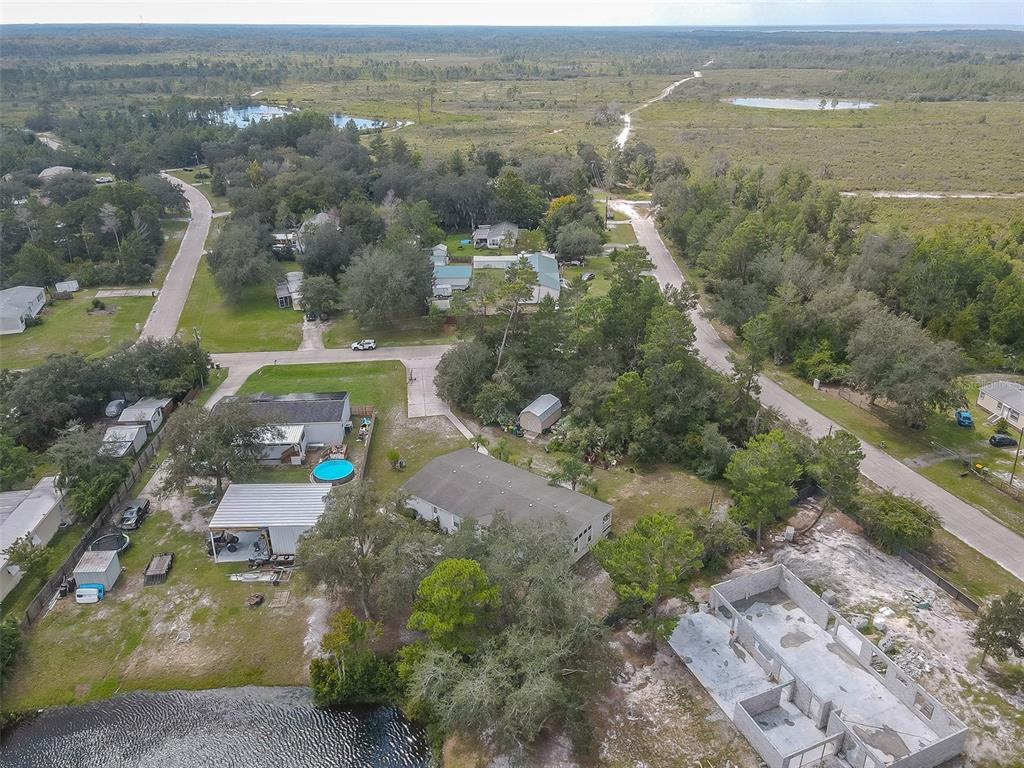 Aerial view of a gray-roofed home among trees, with a pool and wetlands nearby.