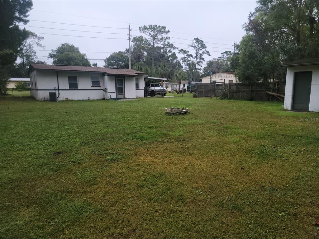 Grassy backyard behind a single-story home, with a small fire pit and detached shed.