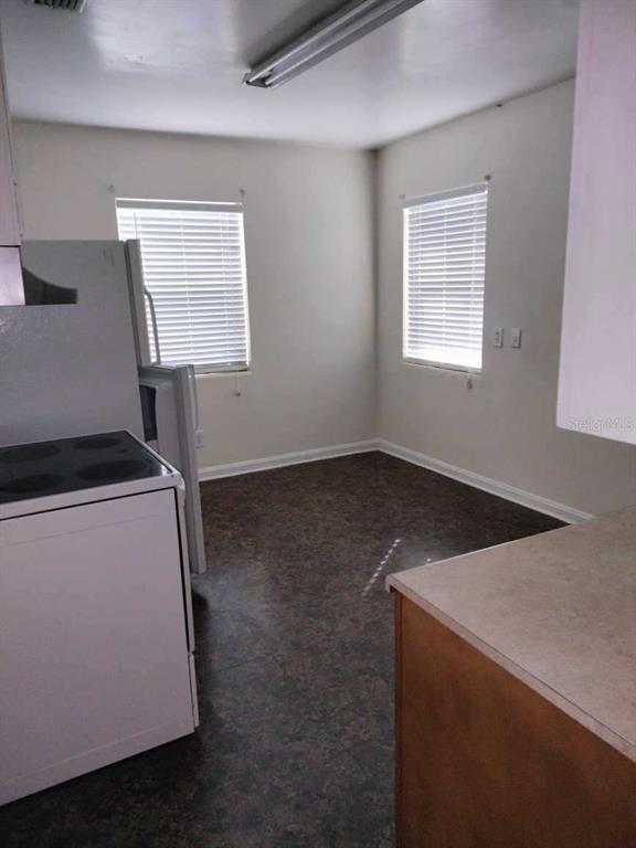 Empty kitchen with white appliances, dark flooring, and two windows with blinds.