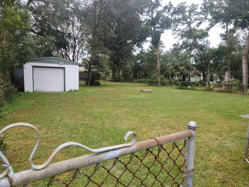 Grassy backyard with a detached white garage, mature trees, and chain-link fencing.
