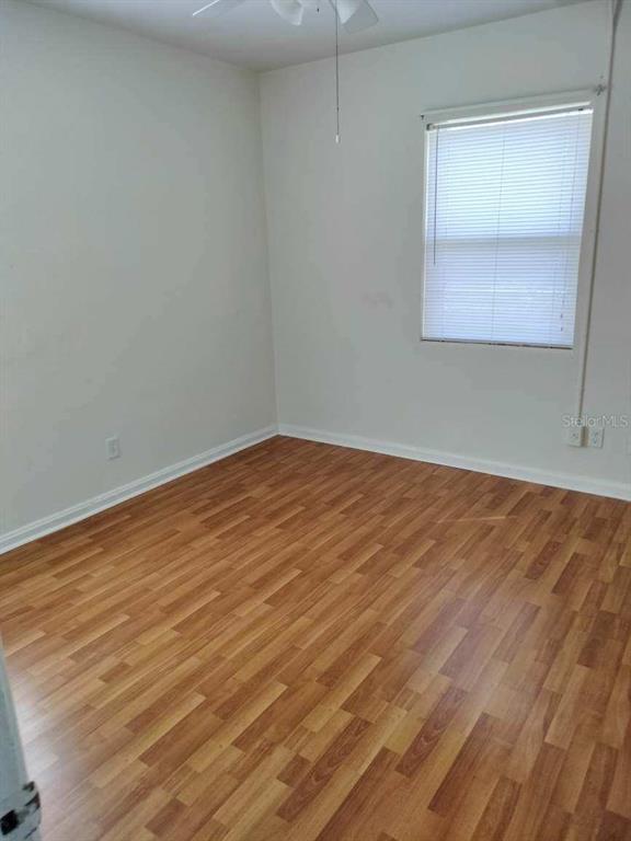 Empty bedroom with wood-look flooring, closed window blinds, and a ceiling fan.