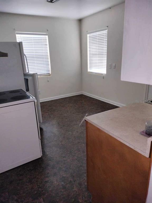 Vacant kitchen with a white stove, two blinded windows, dark flooring, and a wood-front peninsula.