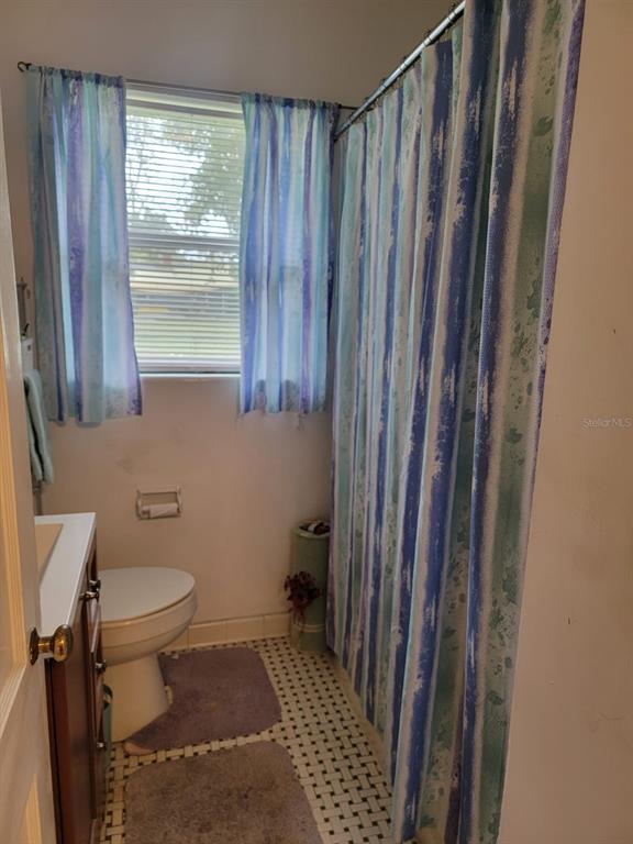 Bathroom with a white toilet, striped blue-green shower curtain, and patterned tile floor.