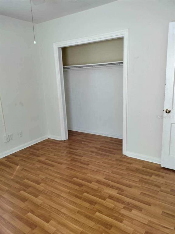 Empty room with wood-look flooring and an open closet.