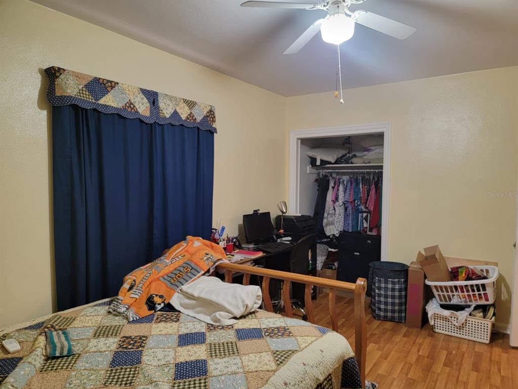 Bedroom with a patchwork bedspread, dark blue curtains, desk, and open clothes closet.