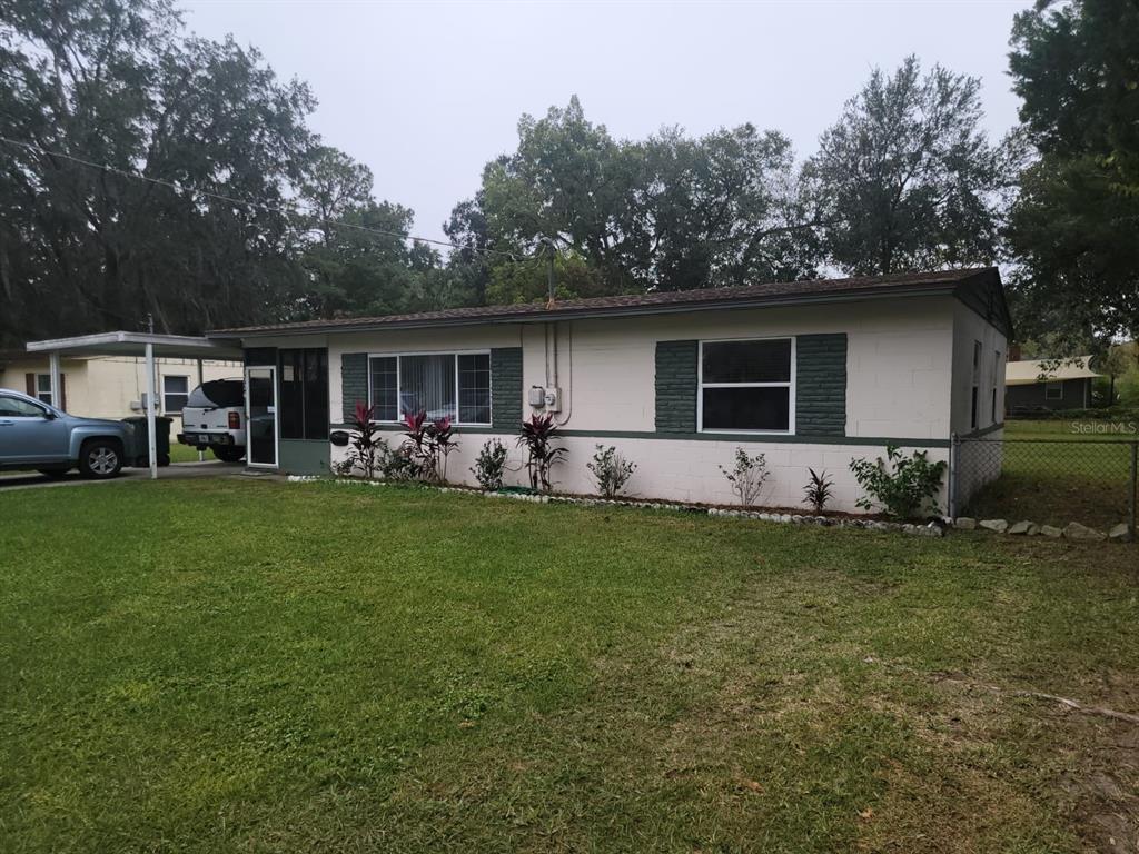 Single-story home with dark green shutters, a broad lawn, and a covered carport.