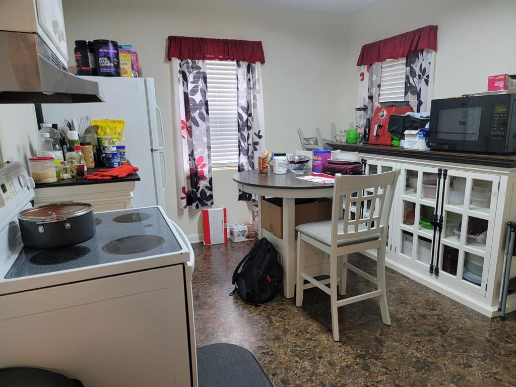 Kitchen with a white stove, round table, and glass-front cabinets beneath two curtained windows.