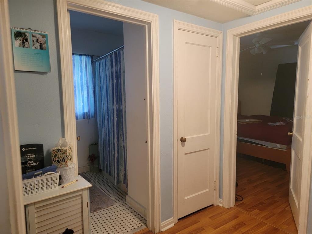 Hallway opening to a tiled bathroom with blue shower curtains and a bedroom with hardwood floors.