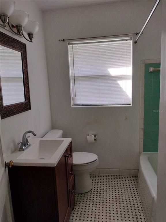Bathroom with dark wood vanity, mosaic tile floor, and bathtub with green tile surround.