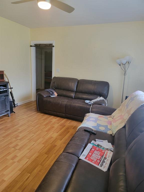 Living room with brown leather sofas, wood-pattern flooring, and a ceiling fan.