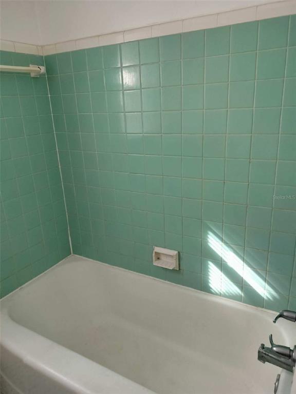 Bathroom bathtub with mint-green tiled walls and a built-in soap dish.
