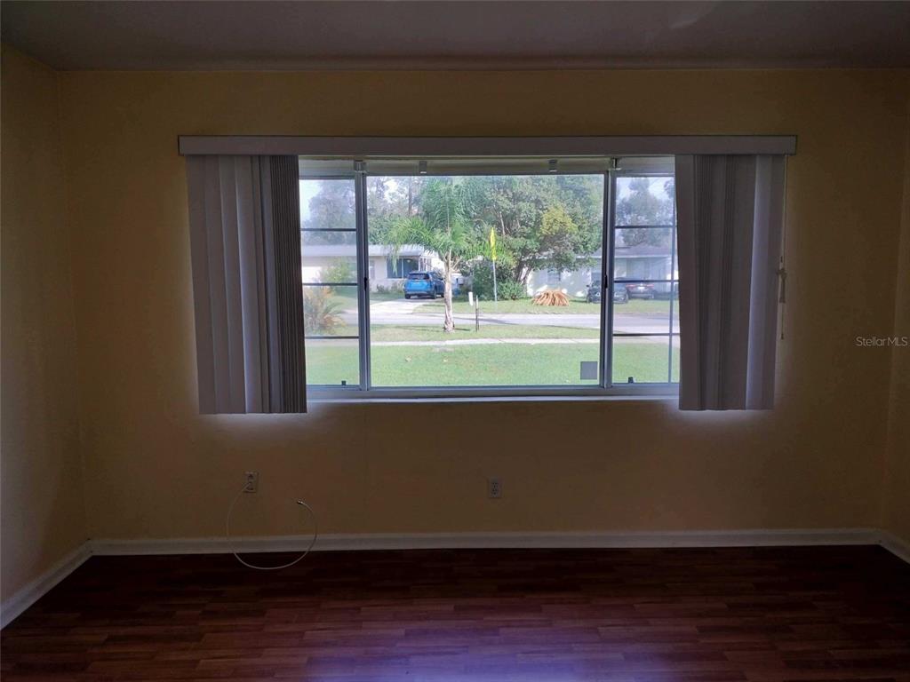 Unfurnished room with dark wood flooring and a large window overlooking the lawn.