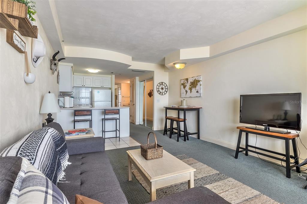Condo living room with a gray sectional, coffee table, television, and open kitchen.