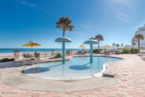 Resort pool with mushroom fountains, palm trees, and the ocean beyond.