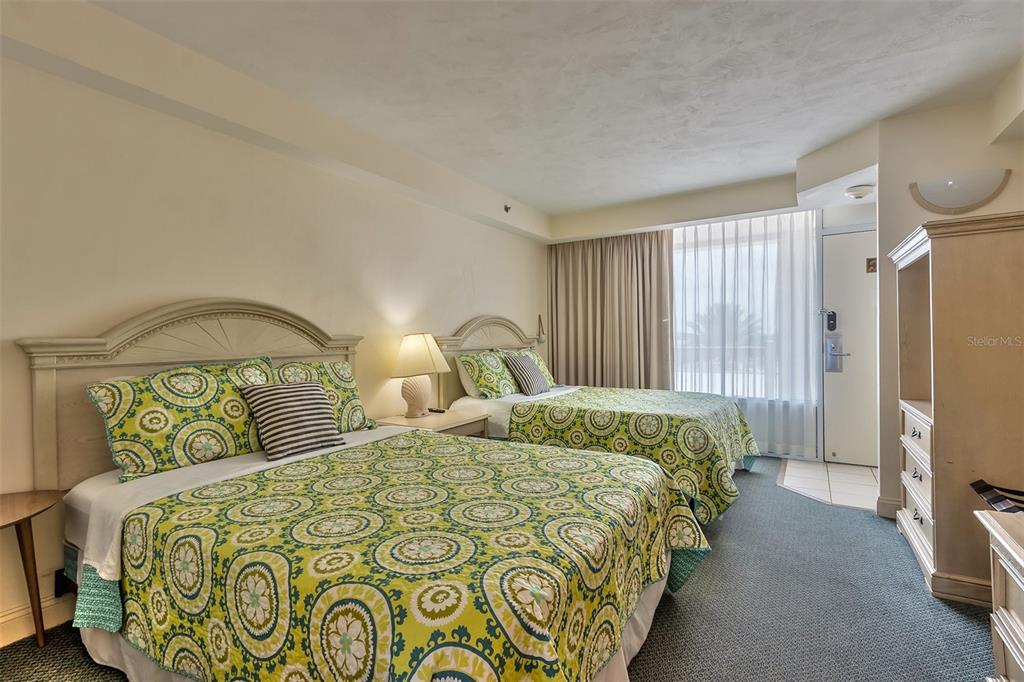 Bedroom with two matching patterned beds, a bedside lamp, and a sliding glass door.