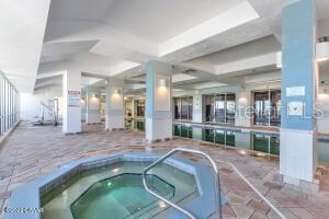 Indoor condominium pool with tiled deck, metal handrails, and glass walls.