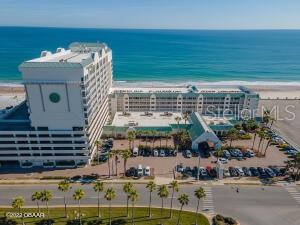 Beachfront condominium complex beside the ocean, with a pool and parking area visible from above.