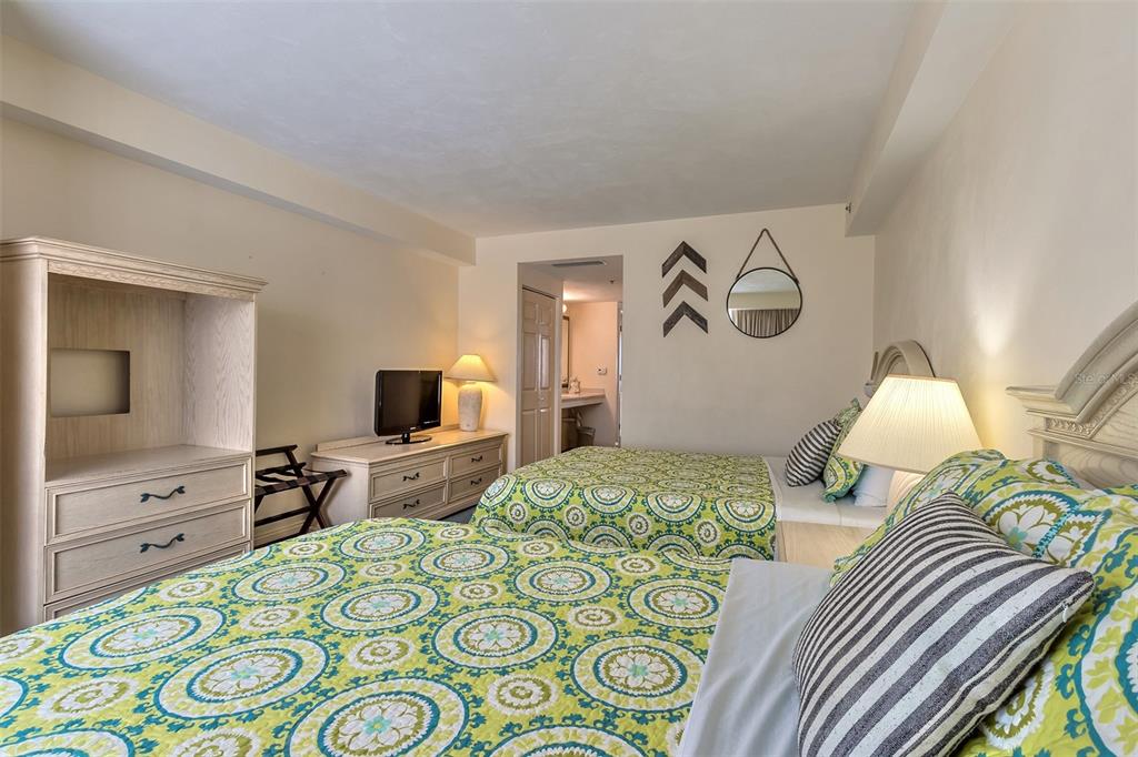 Bedroom with two beds in green patterned bedding and an open doorway to the bathroom.