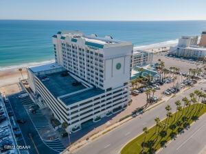 Aerial view of an oceanfront condominium with a swimming pool, beach, and palm-lined coastal road.