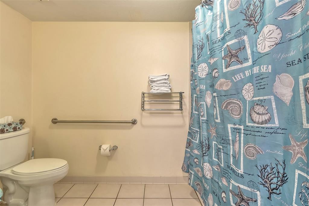 Bathroom with a blue seashell-patterned shower curtain and folded towels on a metal rack.