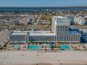 Aerial view of a beachfront condominium with two pools beside a wide sandy beach.