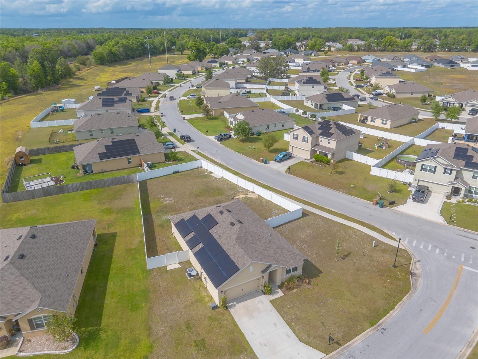Aerial view of a neighborhood with fenced homes, solar panels, and a curving street.