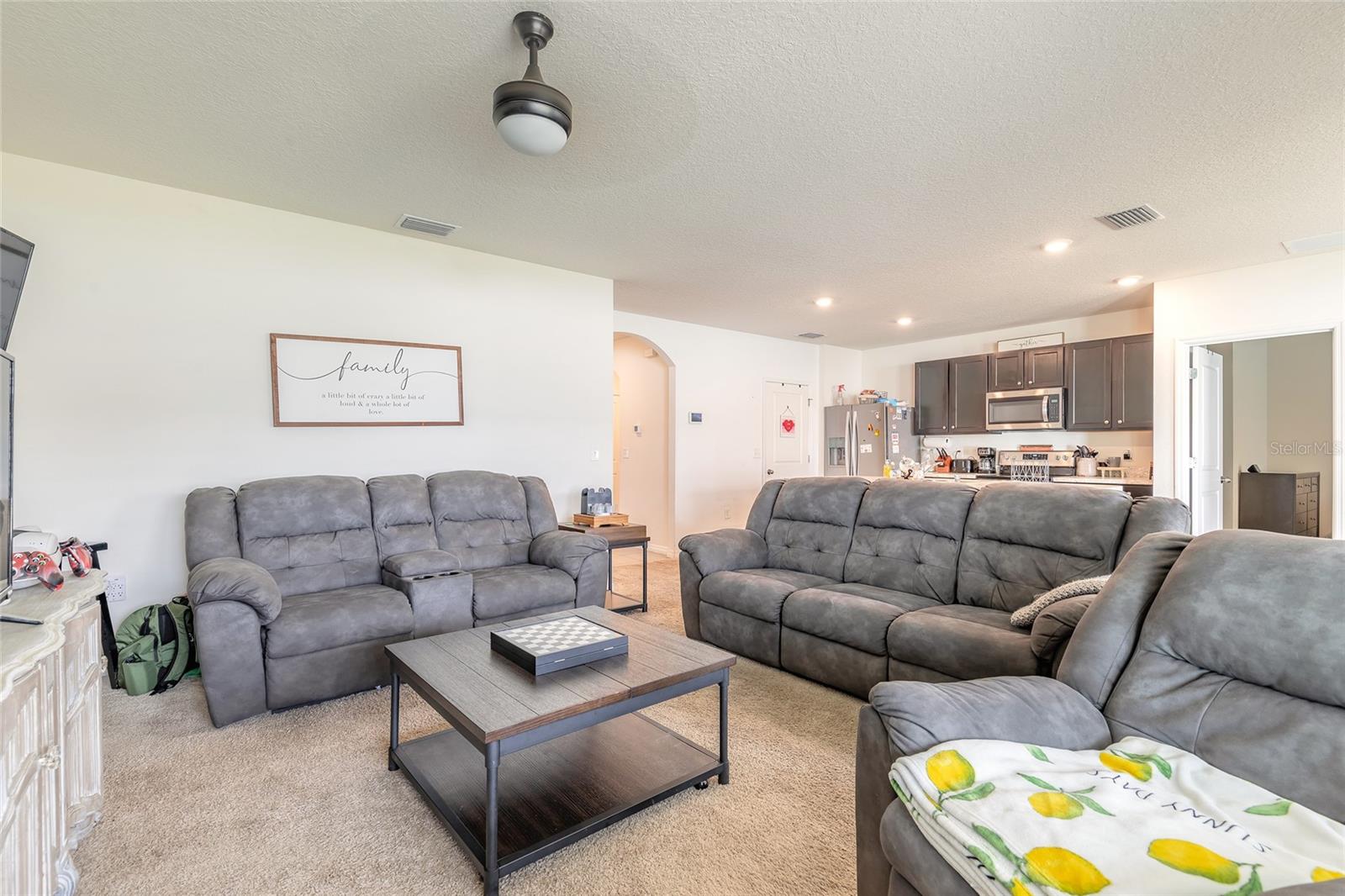 Furnished living room with gray reclining sofas, a coffee table, and an open kitchen.