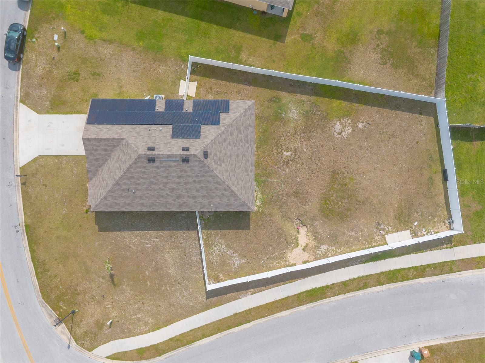 Aerial view of a home with rooftop solar panels and a large fenced backyard.