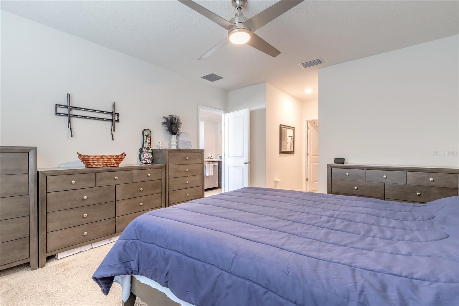 Bedroom with a blue quilted bed, dark dressers, and an open doorway to the bathroom.