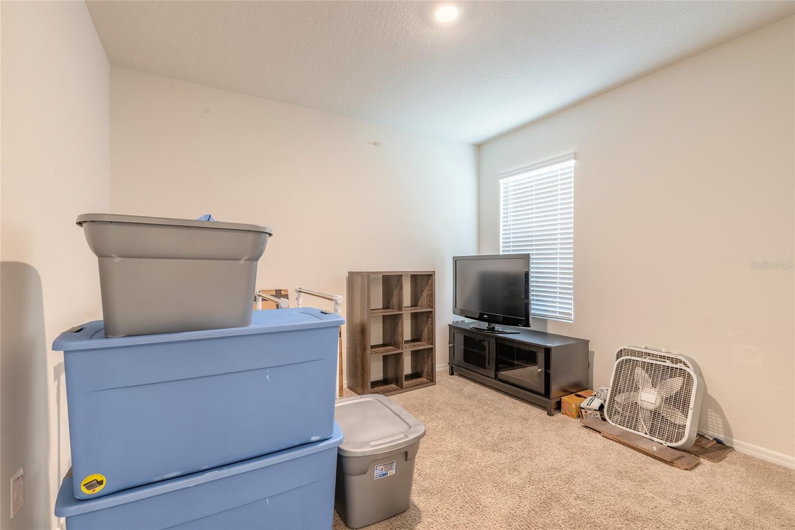 Carpeted room with a television, cube shelf, stacked storage bins, and a box fan.