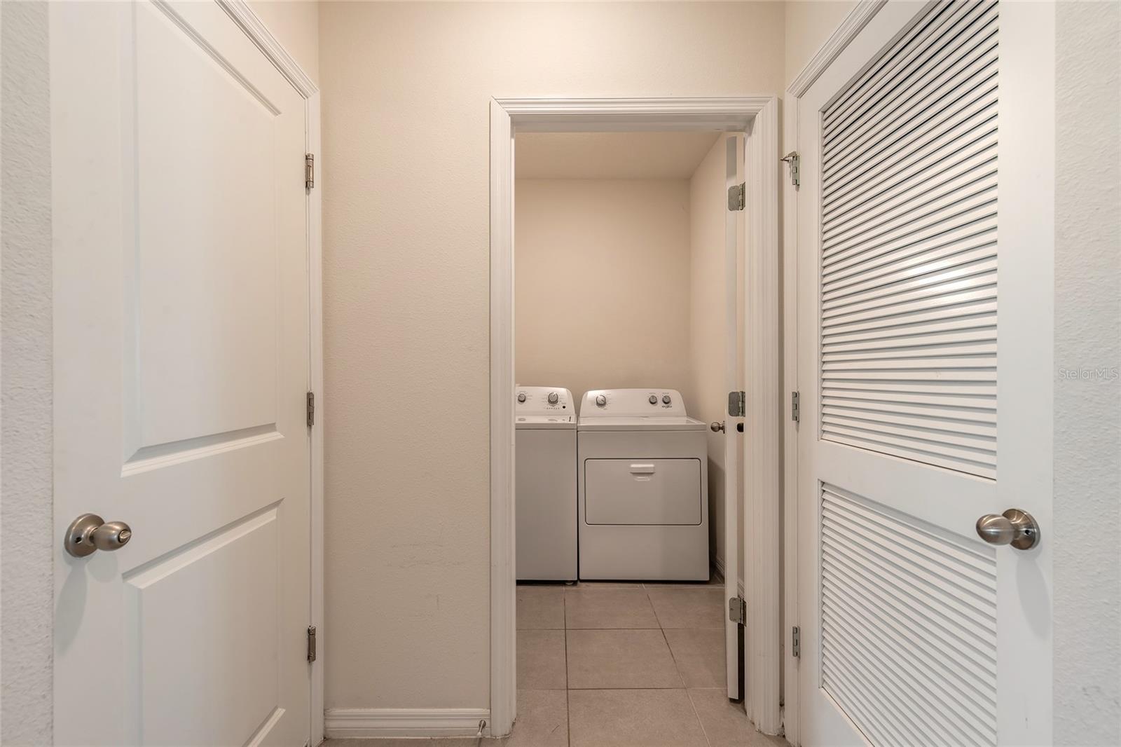 Laundry closet with a white washer and dryer behind open doors.