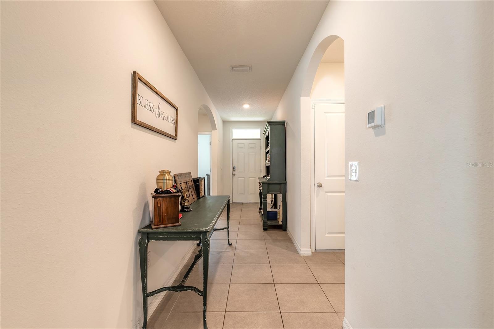 Furnished hallway with beige tile floors, a console table, arched openings, and a front door.