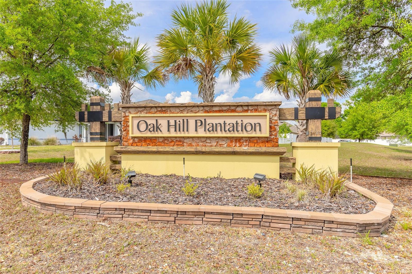 Oak Hill Plantation community entrance sign framed by palm trees and landscaped grounds.