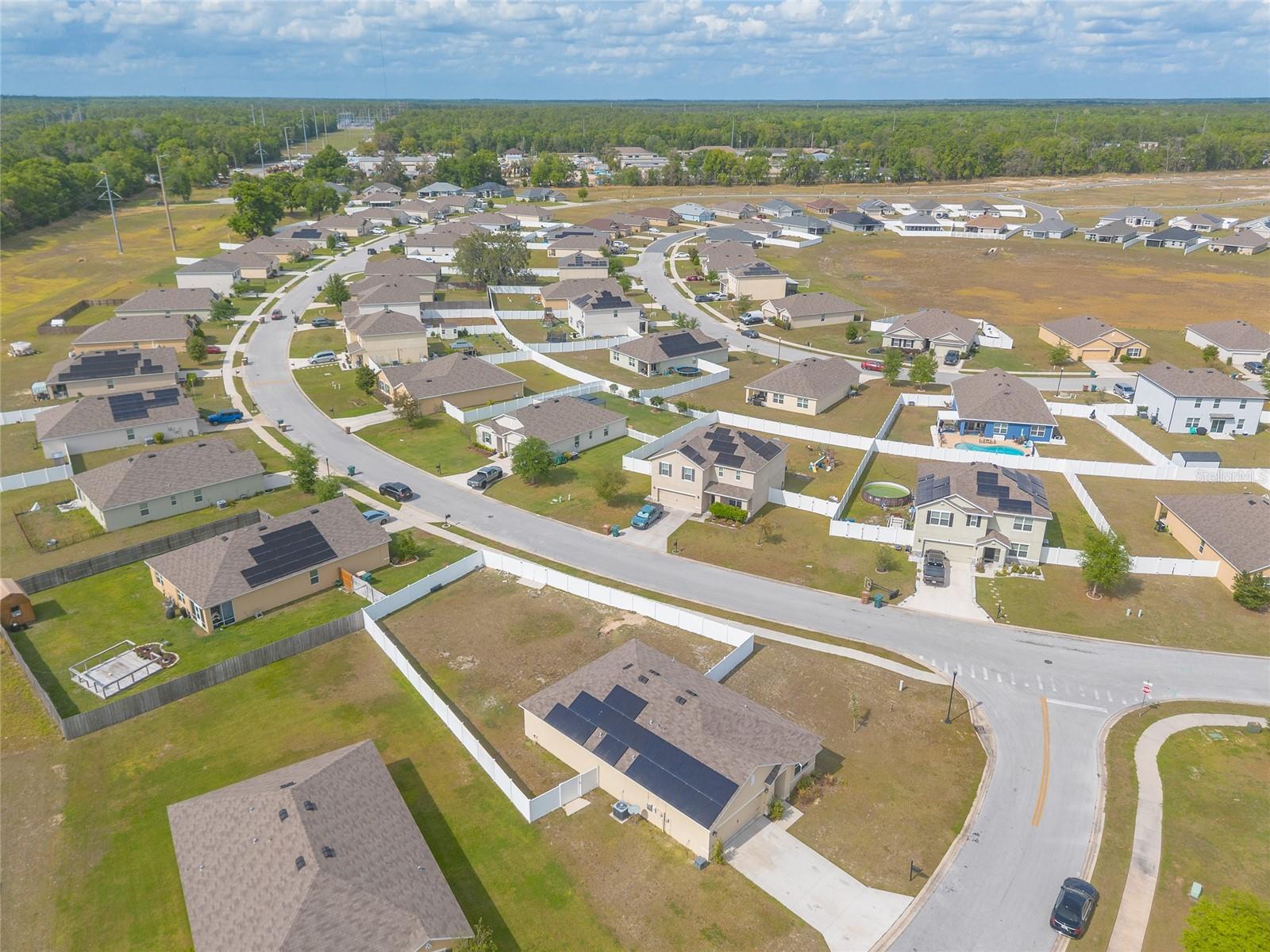 Aerial view of a residential neighborhood with fenced yards, solar panels and a backyard pool.