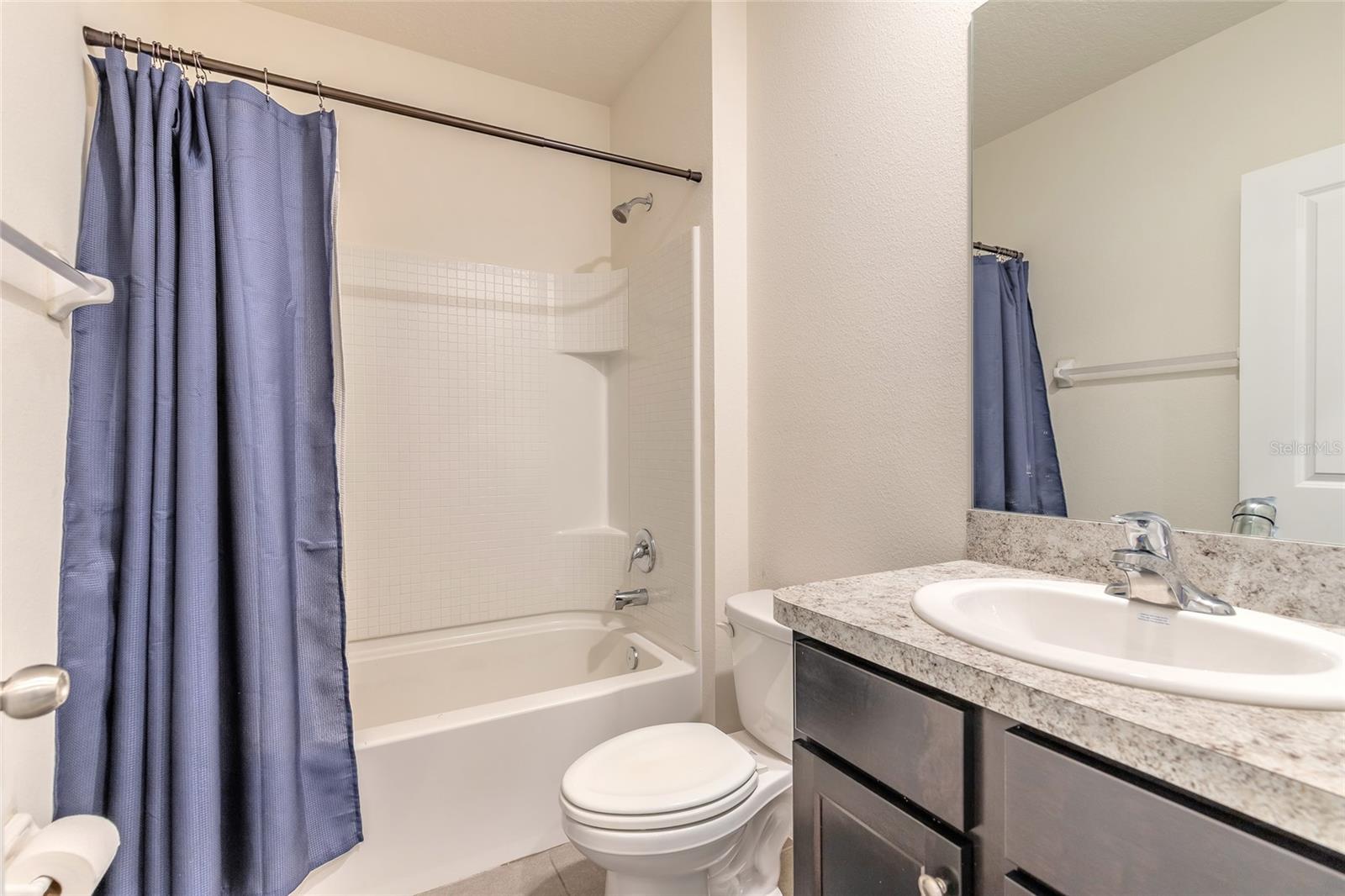 Bathroom with a blue shower curtain, white tub, toilet, and dark vanity with a large mirror.