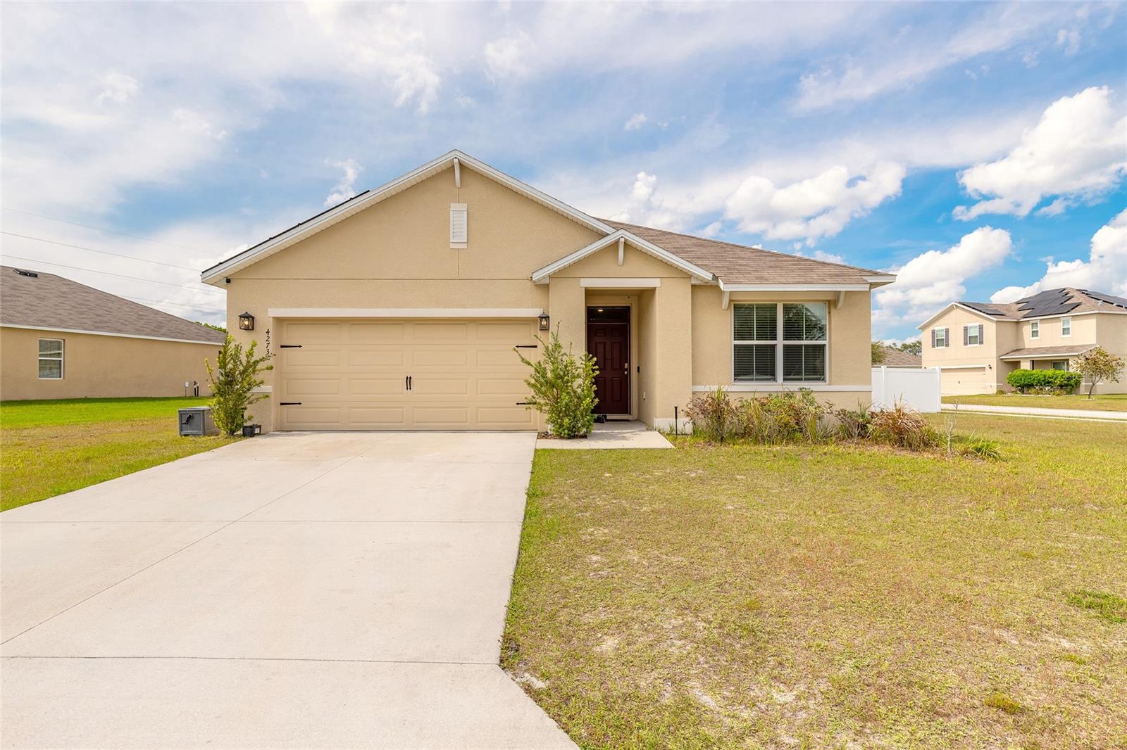 Single-story beige home with a two-car garage, broad driveway, and landscaped front entry.