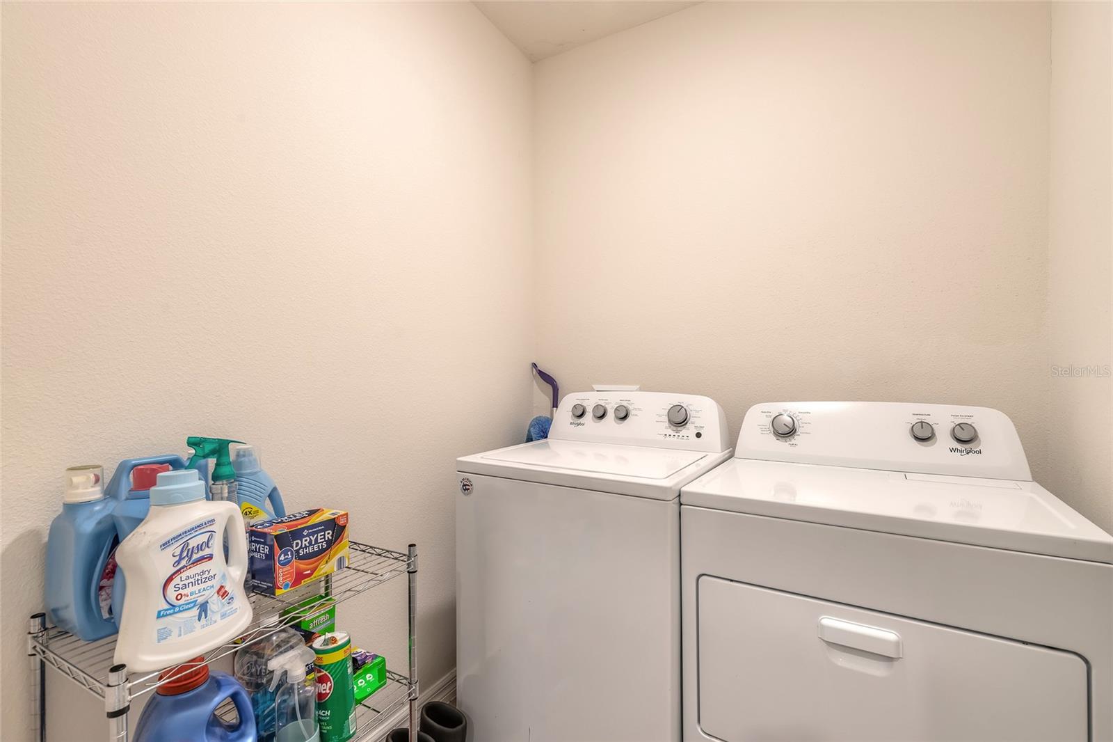 Laundry room with a white washer and dryer beside a wire shelf stocked with laundry supplies.