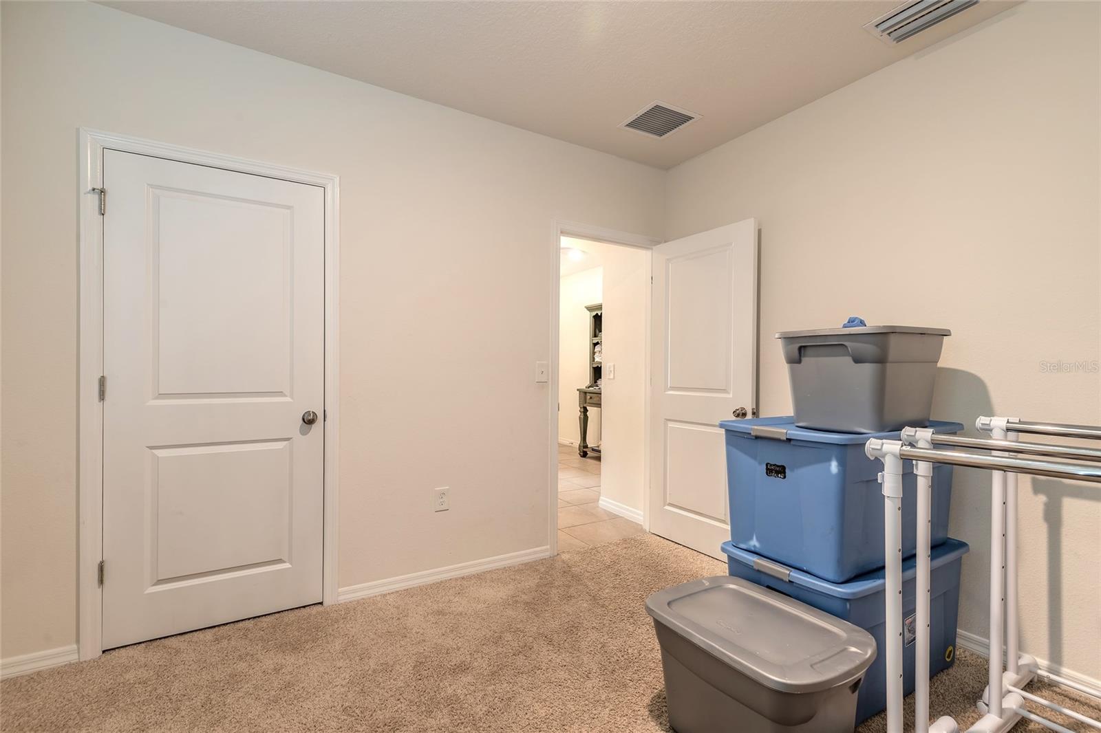Carpeted storage room with stacked plastic bins, a drying rack, and an open doorway to a tiled hall.