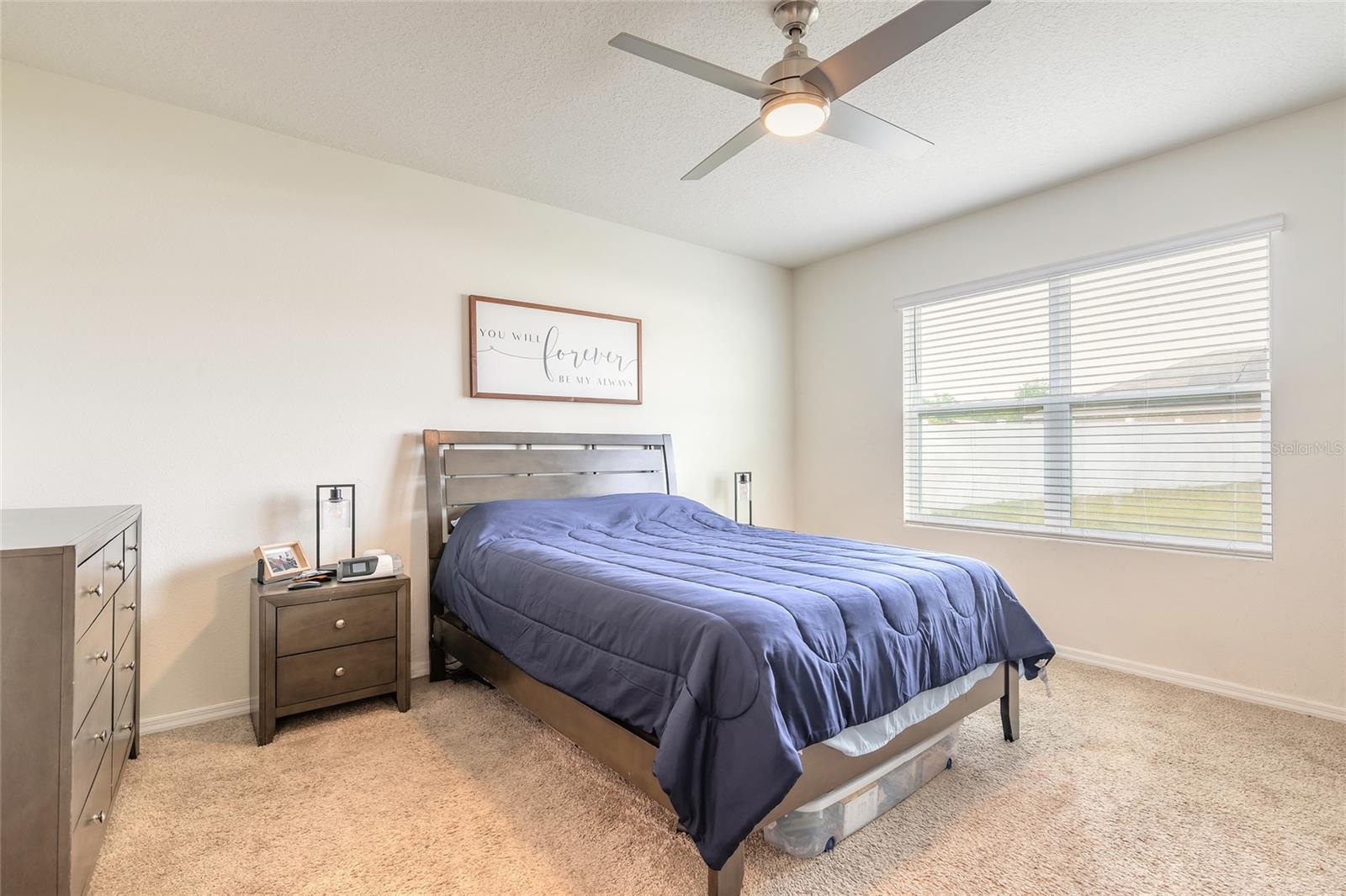 Furnished bedroom with a blue comforter, dark wood bed, and large window with blinds.